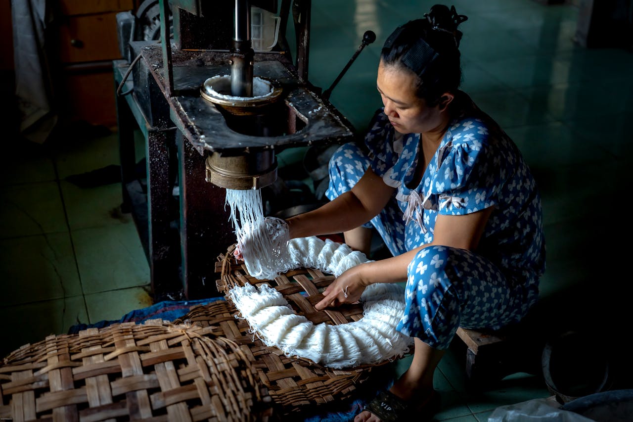 our-experience A woman manually processing cassava starch indoors using traditional equipment.