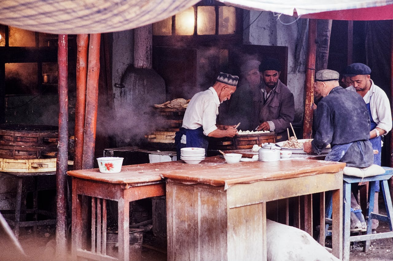 A group of men prepare dumplings in a traditional Chinese kitchen setting.