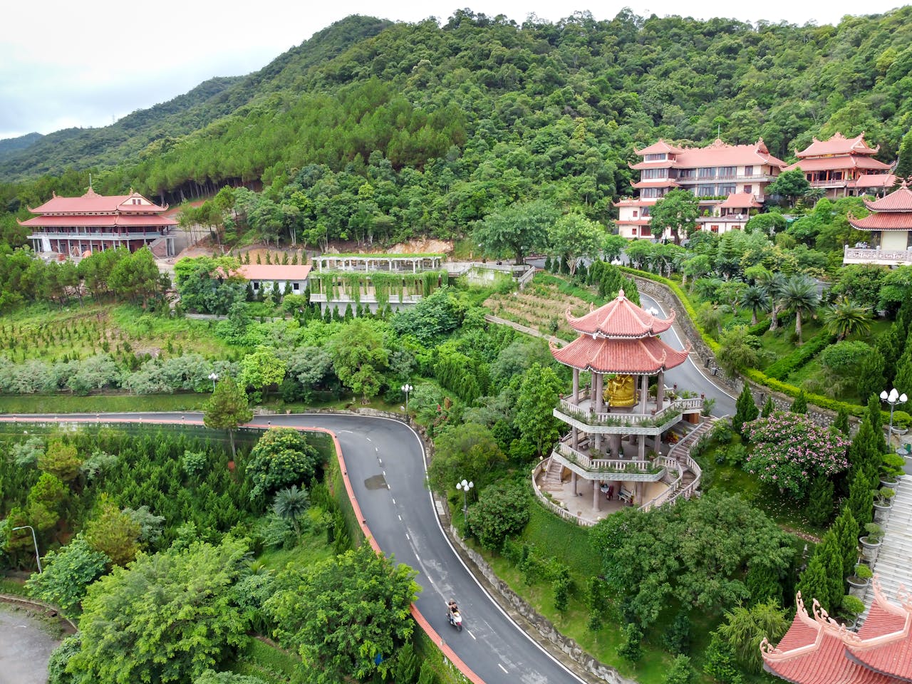 ours-journey A scenic aerial shot showcasing a Vietnamese temple complex surrounded by lush green hills and forests.
